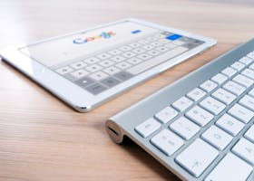 A modern tablet displaying a search engine logo next to a wireless keyboard on a wooden desk.